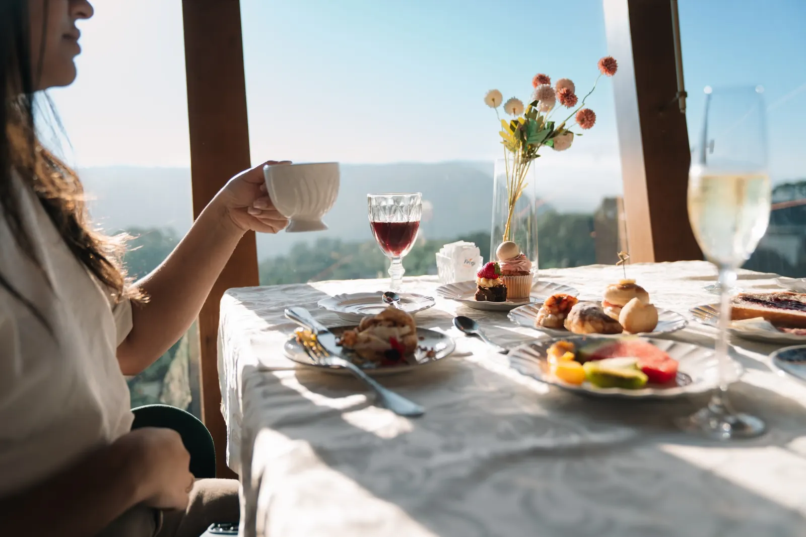 Pessoa tomando café à mesa, junto à janela panorâmica