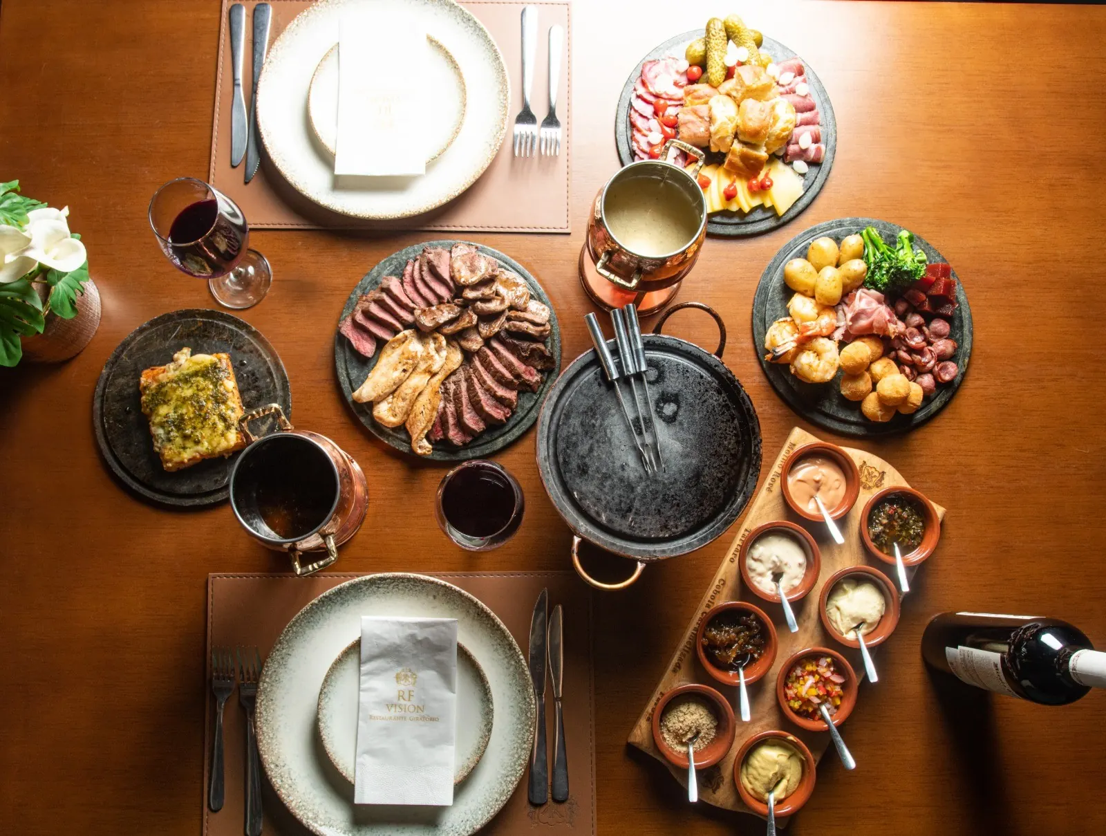 Mesa do fondue vista de cima, com carnes, molhos e acompanhamentos